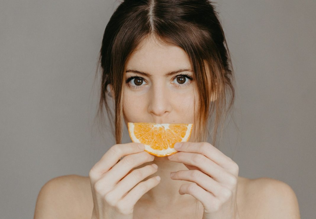 A woman holding an orange slice in front of her face